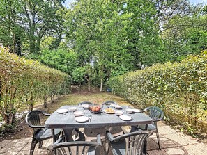 Een tafel buiten opstelling met stoelen, omgeven door begroeiing en bomen.