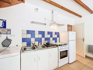 Cozinha compacta com armários brancos, painel de azulejos azul e branco, pia de aço inoxidável, fogão e geladeira.