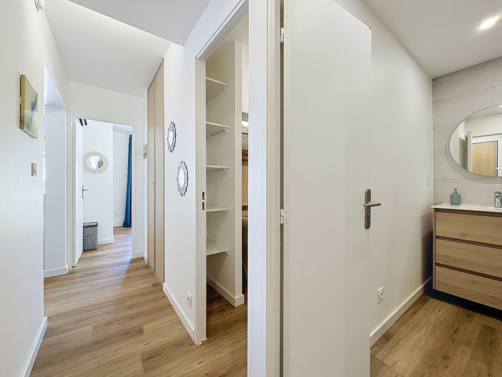 A hallway with wooden flooring, white walls, and a partially open closet door.
