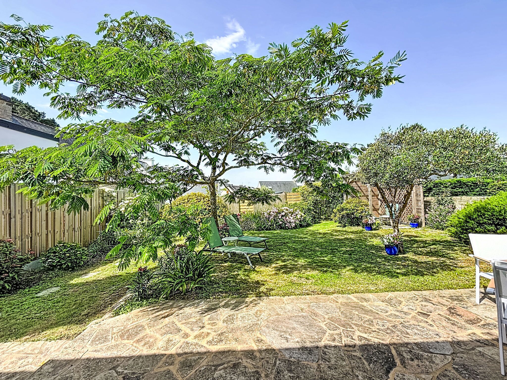 Un jardin avec une terrasse en pierre, une pelouse verdoyante et une clôture en bois.