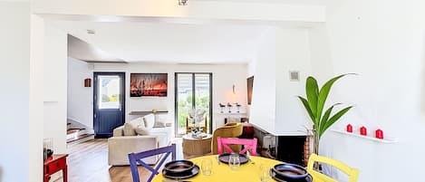 A dining area with a yellow table, black and blue plates, and chairs. There is a plant on the right and a window with a view of the outside.