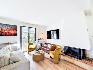 Ein modernes Wohnzimmer mit einer Couch, zwei Sesseln, einem Couchtisch, einem Kamin und einem an der Wand montierten Fernseher.