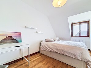 A bedroom with a bed, a desk, a chair, a window, and a picture on the wall. - Maison de Suffren by Interhome (St Gildas-de-Rhuys)