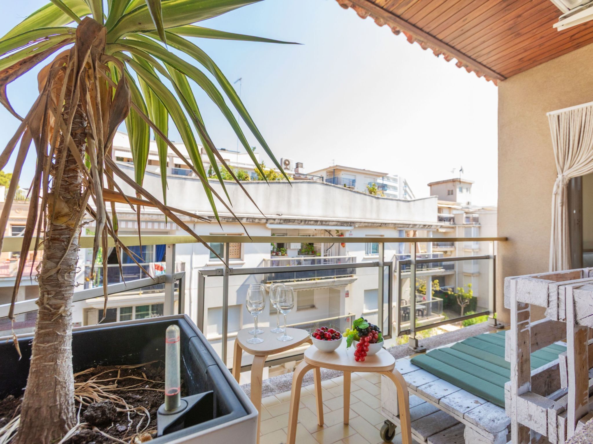 A balcony with a palm tree, a small table with wine glasses, and a bowl of fruit.