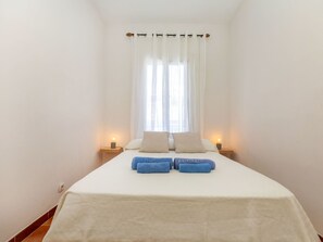 Ein Hotelzimmer mit einem Bett, weißen Vorhängen, zwei Nachttischlampen und einem Fenster mit leichtem Stoff.