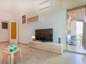 Ein modernes Wohnzimmer mit einem Flachbildfernseher, einem kleinen Tisch mit einer Lampe und einer Schiebetür zum Balkon.