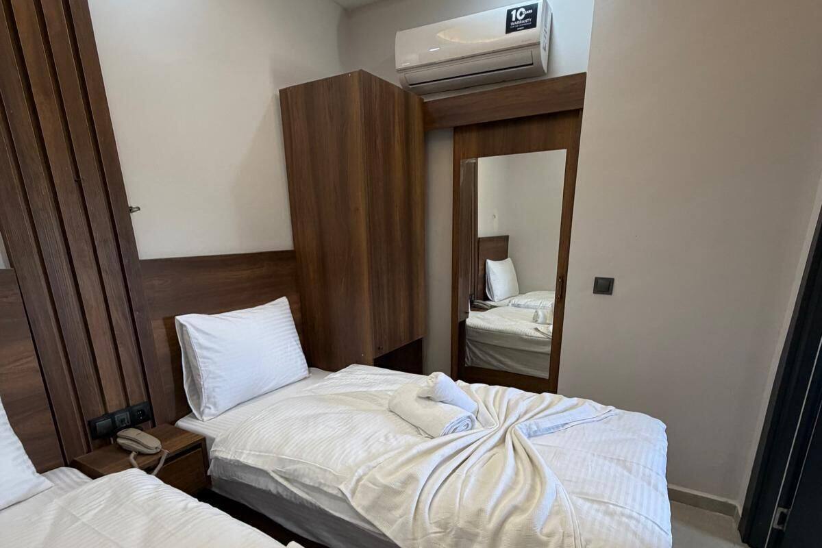 A hotel room with two beds, a wooden headboard, a bedside table with a phone, and an air conditioning unit.