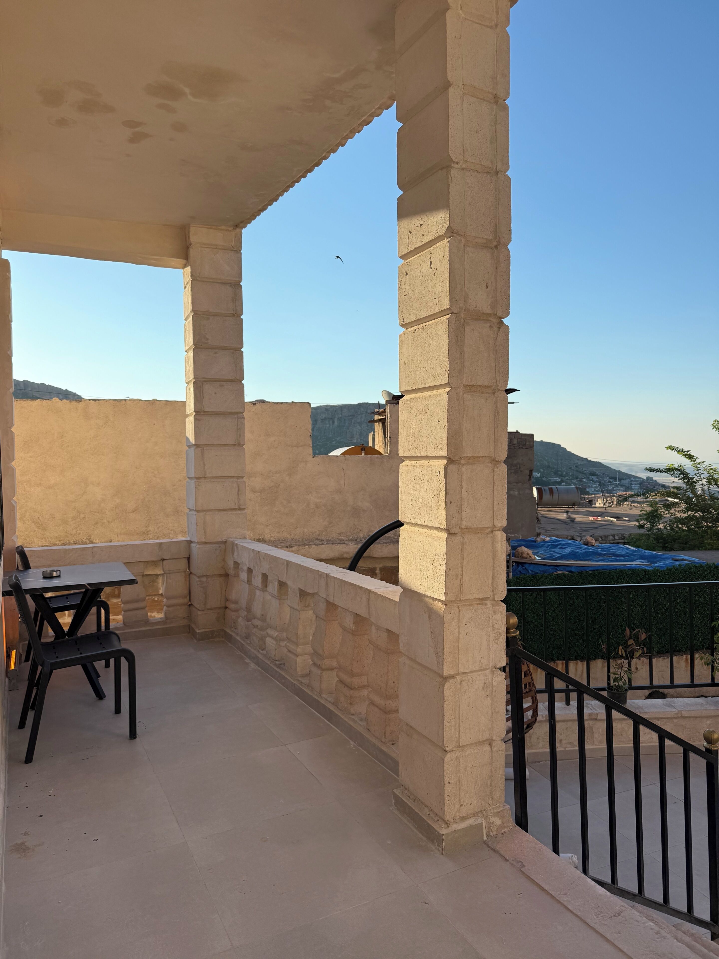 Un balcón con mesa y sillas, pilares de piedra y vistas de la ciudad.