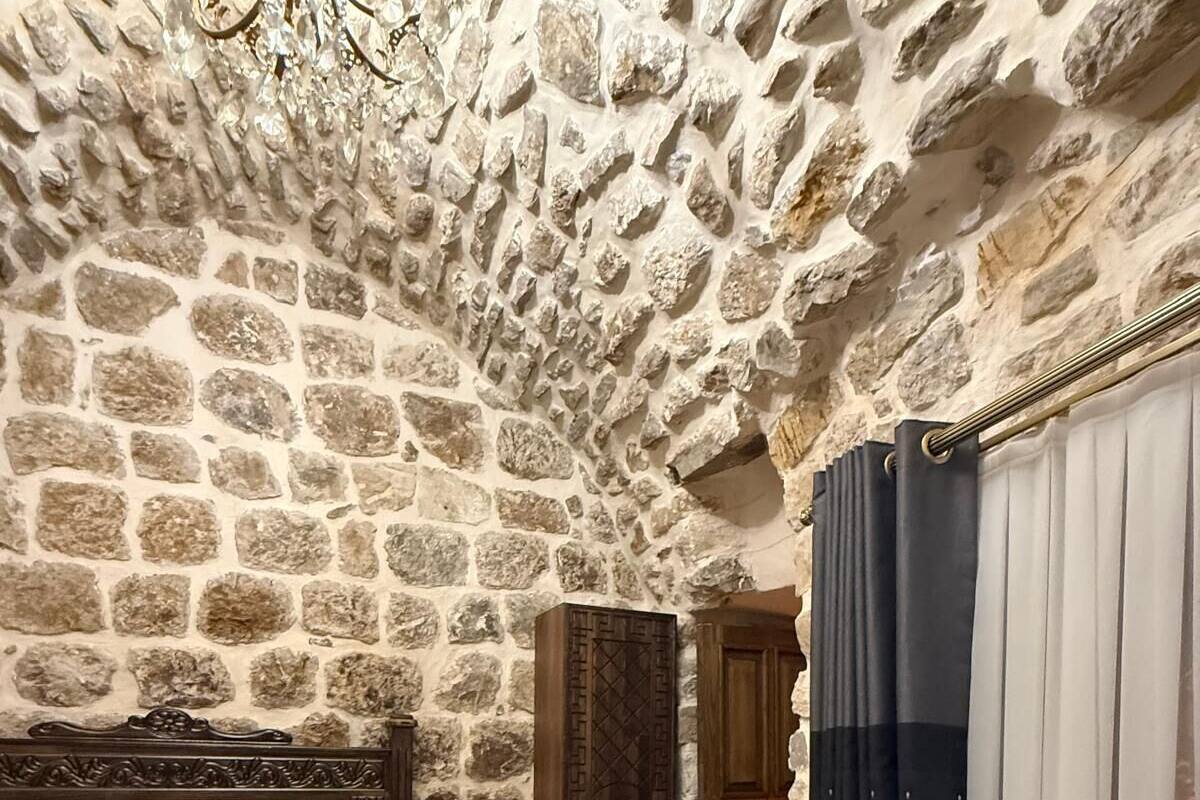A stone-walled bedroom with a bed, a wardrobe, and a door.