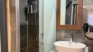 A bathroom with a glass-enclosed shower, a wooden vanity, and a mirror above the sink. - Erkar Konağı (Mardin)