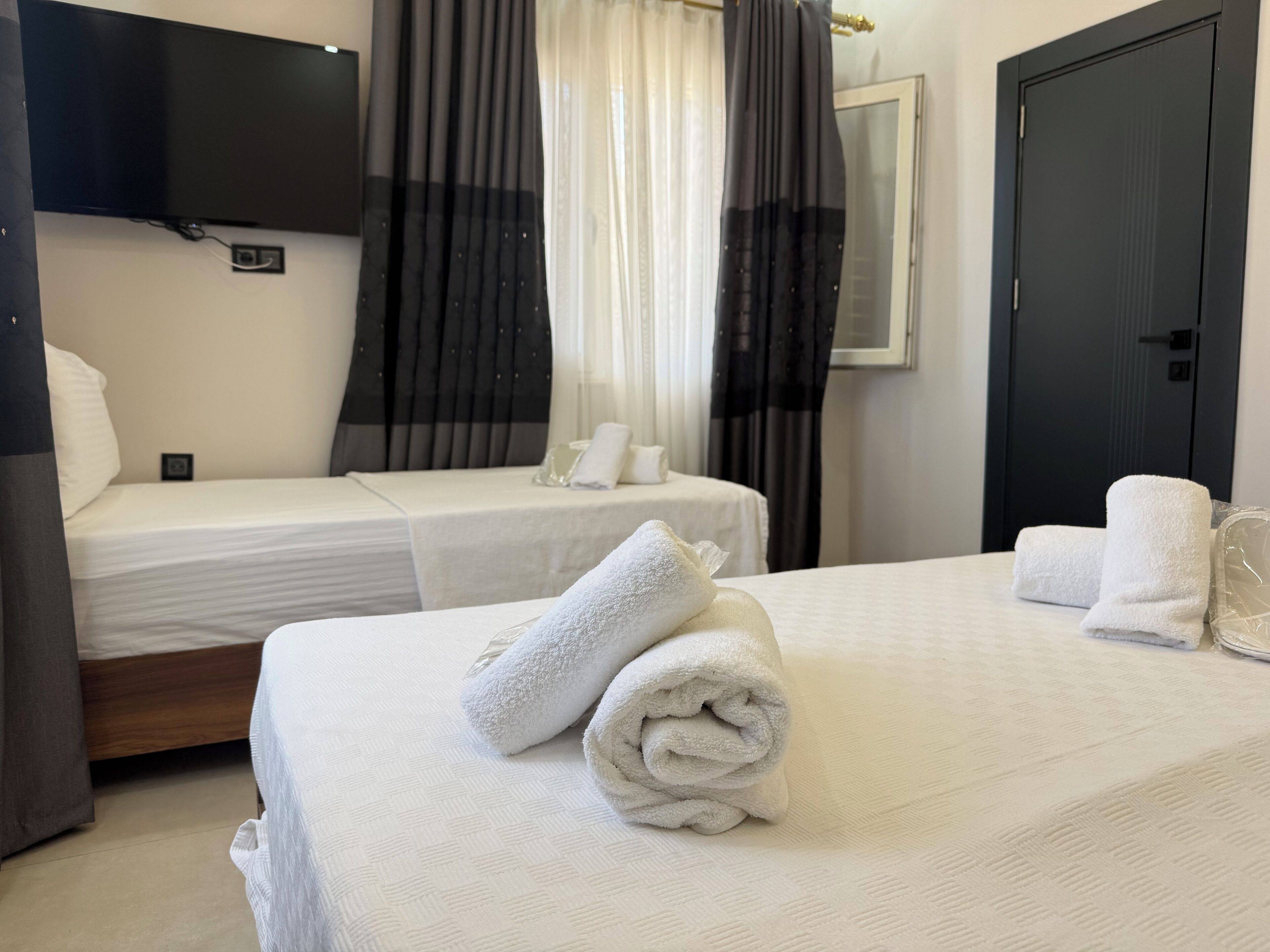 Habitación de hotel con dos camas, un televisor de pantalla plana montado en la pared y una puerta con picaporte.