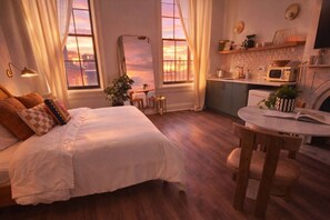 A bedroom with a large bed, a bedside table, a chair, a small table, a window, and a kitchen area with a microwave. - Luxury Queen Studio - Solara at The Marle Boutique Hotel-Near JHU + Downtown (Baltimore)