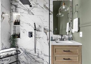 Un bagno con una parete in marmo, un lavandino, uno specchio e un porta asciugamani.