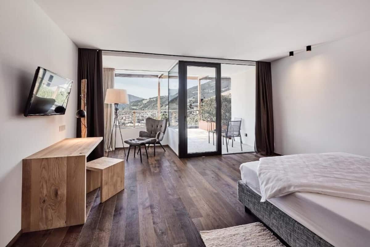 Une chambre d’hôtel moderne dotée d’un grand lit, d’un bureau en bois, d’une télévision et d’un balcon offrant une vue sur la ville.