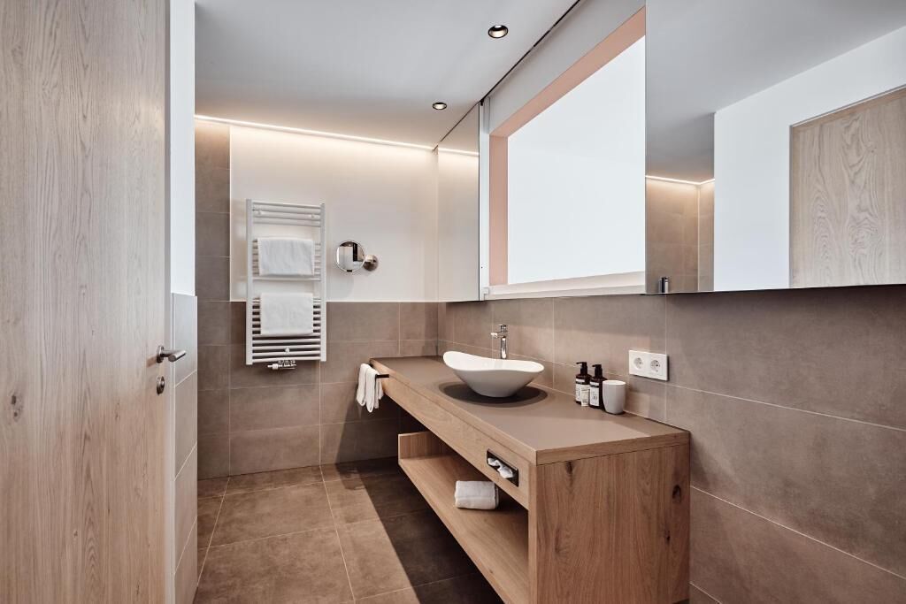 Un baño moderno con tocador de madera, un lavamanos blanco y un espejo grande.