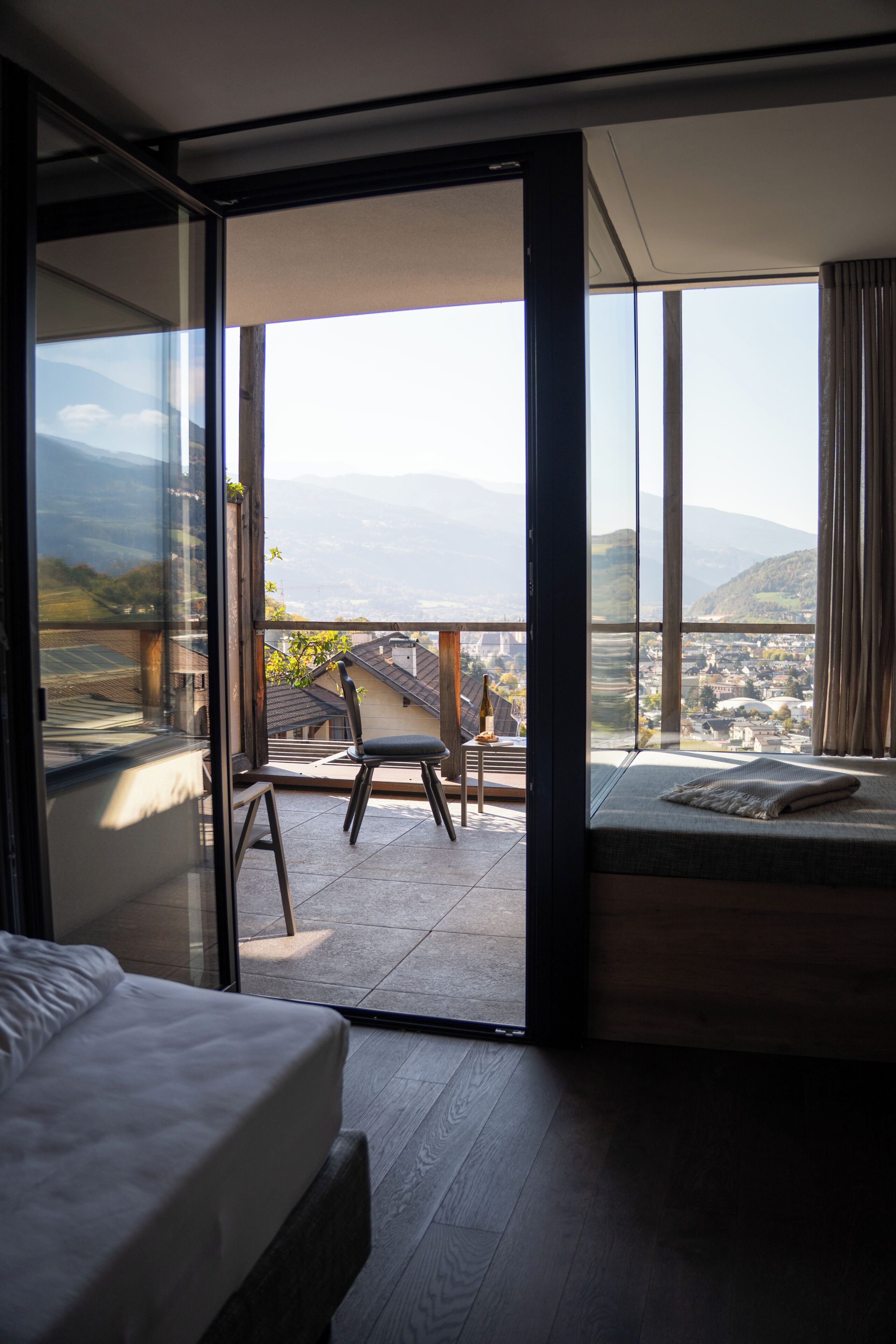 Un dormitorio con un amplio ventanal corredera que da a un balcón con vistas a un pueblo y montañas.