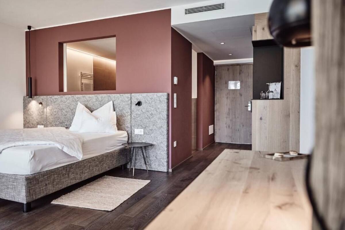 A modern bedroom with a large bed, a bedside table, a mirror, and a wardrobe.