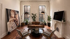 A living room with a brown leather sofa, two armchairs, a coffee table, a painting, and a fireplace. - Serenité King Studio+Sleeper Sofa | Near JHU & DT (Baltimore)