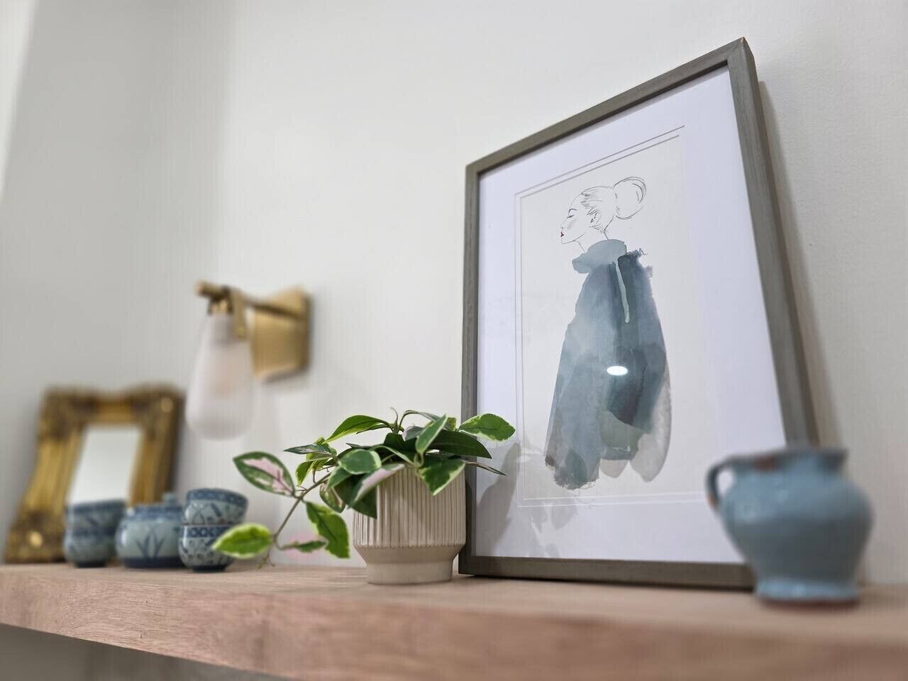 A framed artwork on a shelf, a potted plant, and decorative vases.