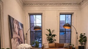 A room with a dark wooden table, a white bust sculpture, a large painting, a brown leather sofa, and two floor lamps. - Serenité King Studio+Sleeper Sofa | Near JHU & DT (Baltimore)