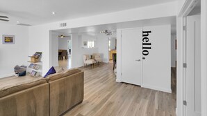 A modern interior with a wooden floor, a beige sofa, a white door with 'hello' on it, and a hallway leading to a dining area. - Scottsdale Oasis Diving Pool, Game Room & 4BR Near Old Town & Mayo Clinic (Scottsdale)
