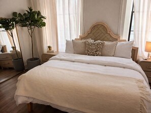 A neatly made bed with a headboard, bedside tables, and potted plants. - Amour Luxury King Suite w/ Soaking Tub - Boutique Hotel Near Johns Hopkins & DT (Baltimore)