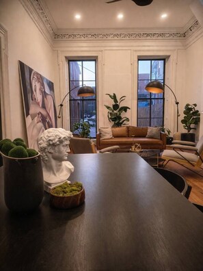 A dining area with a dark wooden table, a white bust sculpture, and a large painting on the wall. - Amour Luxury King Suite w/ Soaking Tub - Boutique Hotel Near Johns Hopkins & DT (Baltimore)