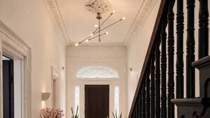 A hallway with a checkered floor, a staircase with black balusters, and a decorative ceiling light fixture.