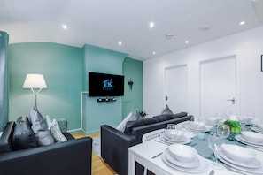 Un salon moderne comprenant un canapé, une table à manger pour six personnes, un téléviseur à écran plat et une porte.