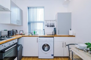 A compact kitchen with a washing machine, a toaster, and a window with blinds. - 4 Guests | 1 Double bed and Sofa Bed (Merseyside)