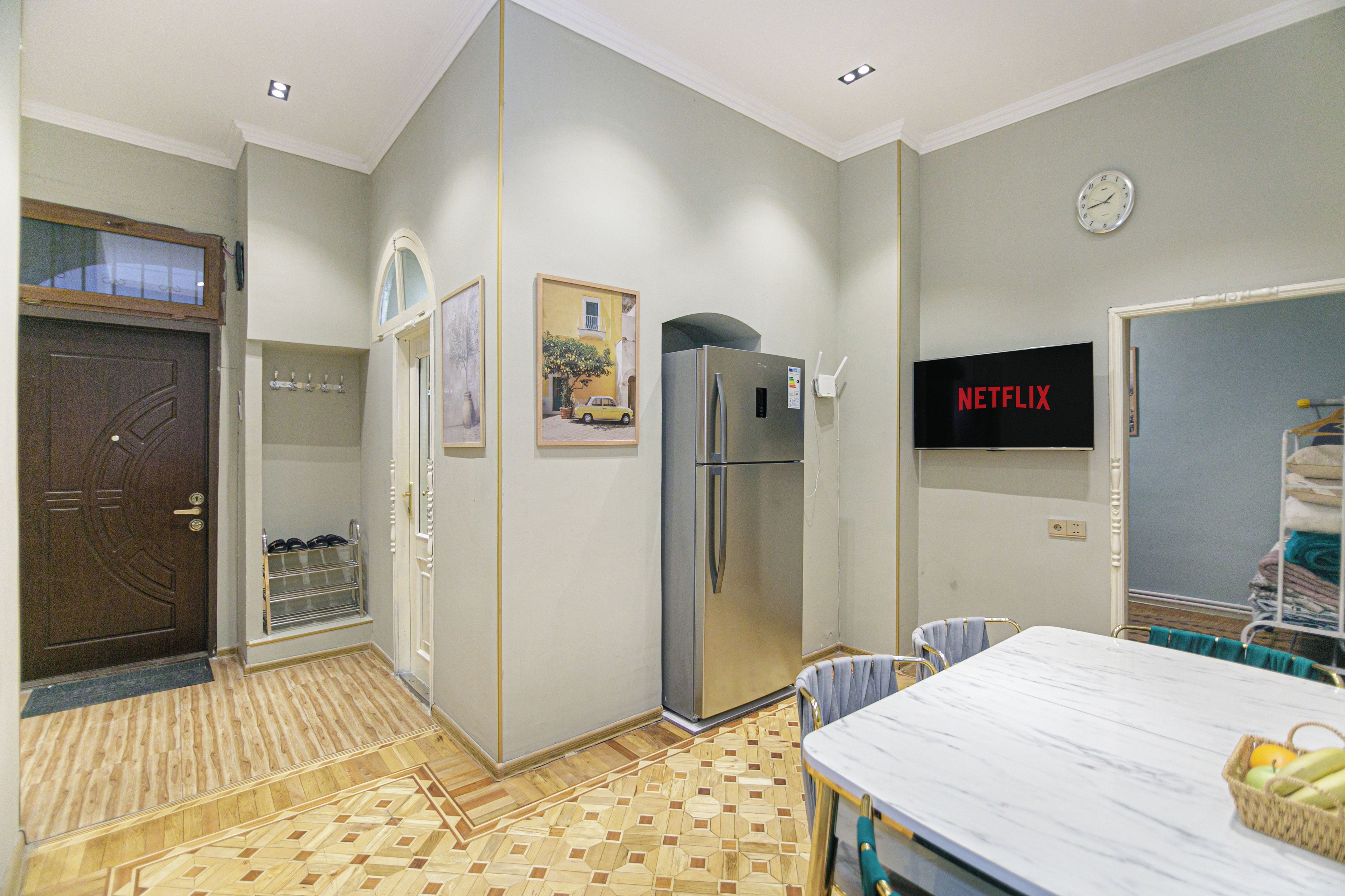 A compact living space with a kitchenette, a refrigerator, a dining table, and a wall-mounted television.