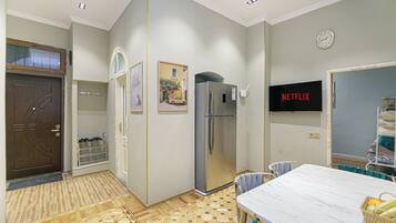 A compact living space with a kitchenette, a refrigerator, a dining table, and a wall-mounted television.