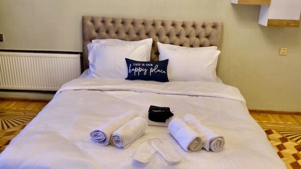 A neatly made bed with rolled towels, a pillow with a message, and two floral artwork pieces on the wall above. - Family Friendly 2BR  w/Balcony - Steps from Old city - 4 min Walk to Nizami (Baku)