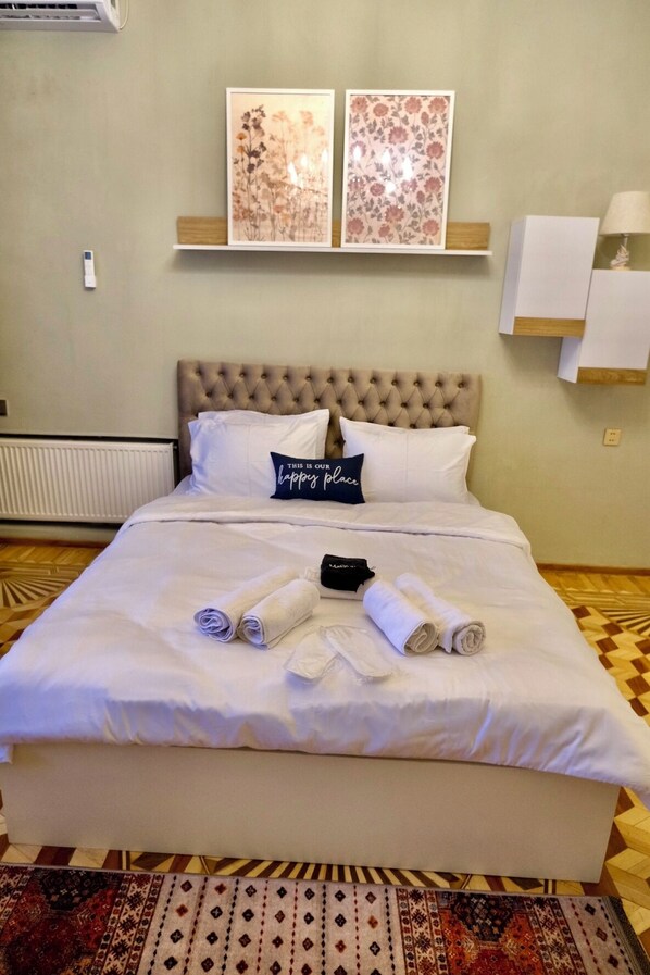 Cama bem arrumada com toalhas dobradas, um travesseiro com mensagem e duas obras de arte floral na parede acima.
