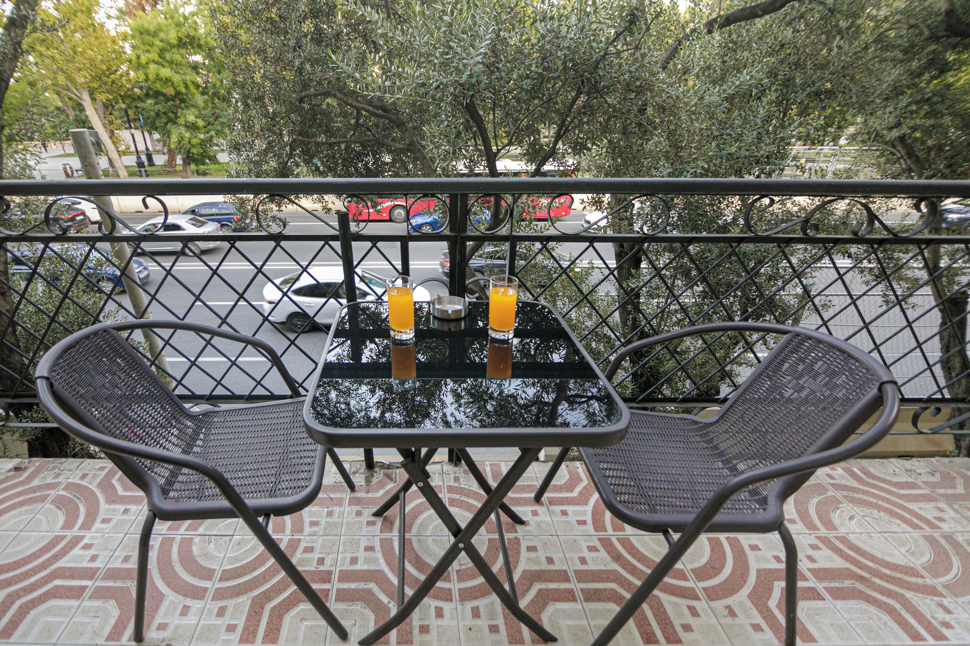 A balcony with two chairs and a table, a glass of orange juice, and a metal bowl.