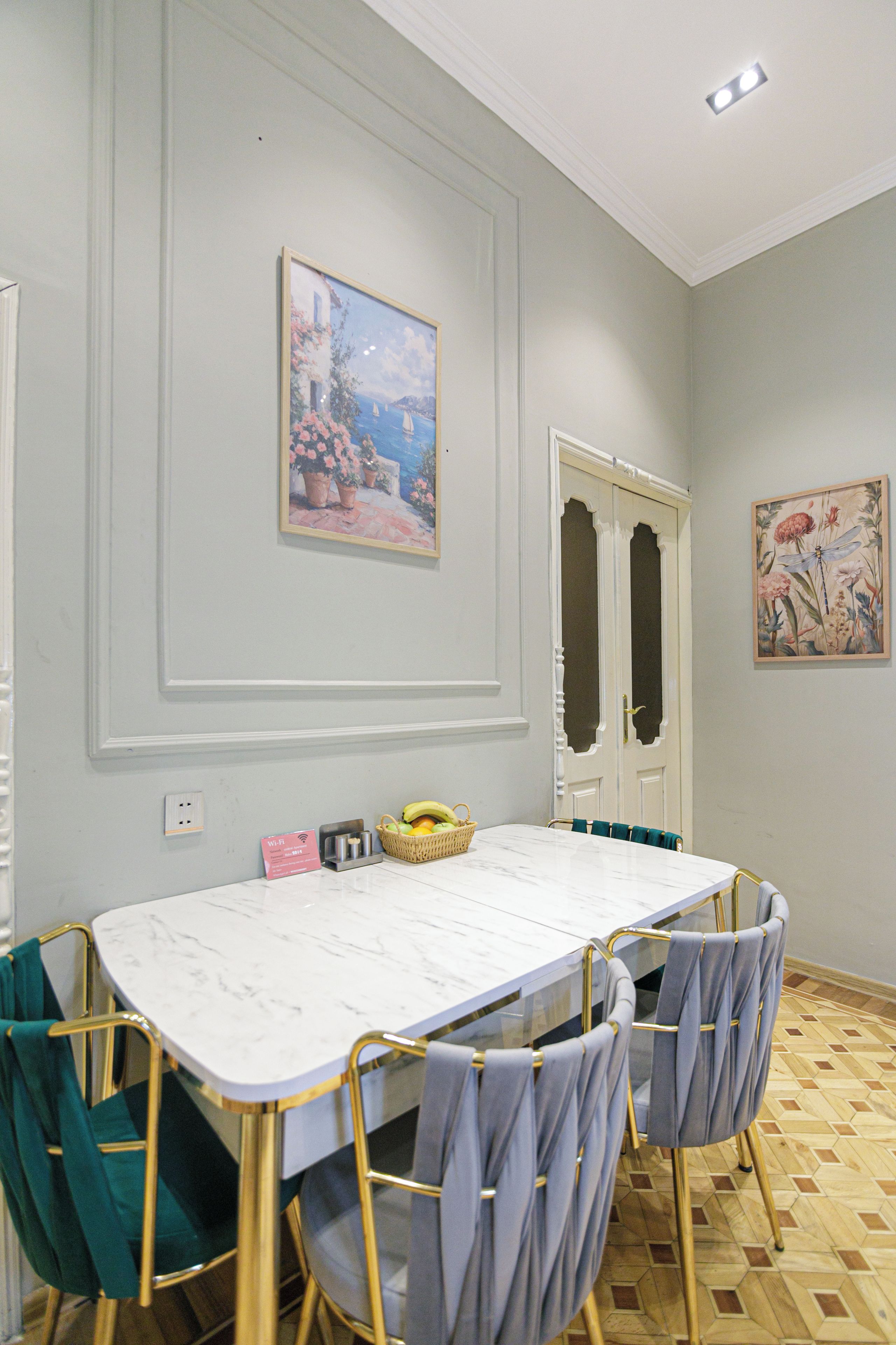 Un comedor con una mesa de mármol, cuatro sillas, una cesta de fruta y un cuadro en la pared.