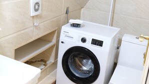 A compact laundry area with a washing machine, a dryer, and a small shelf unit. - Family Friendly 2BR  w/Balcony - Steps from Old city - 4 min Walk to Nizami (Baku)