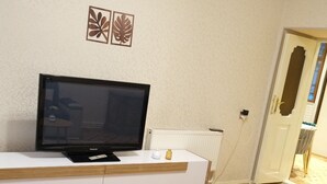A living room with a flat-screen TV on a white entertainment unit, a blue sofa, and a small wooden table with a vase. - Family Friendly 2BR  w/Balcony - Steps from Old city - 4 min Walk to Nizami (Baku)