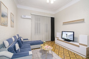 A living room with a sofa, a coffee table, a television, and a patterned floor. - Family Friendly 2BR  w/Balcony - Steps from Old city - 4 min Walk to Nizami (Baku)