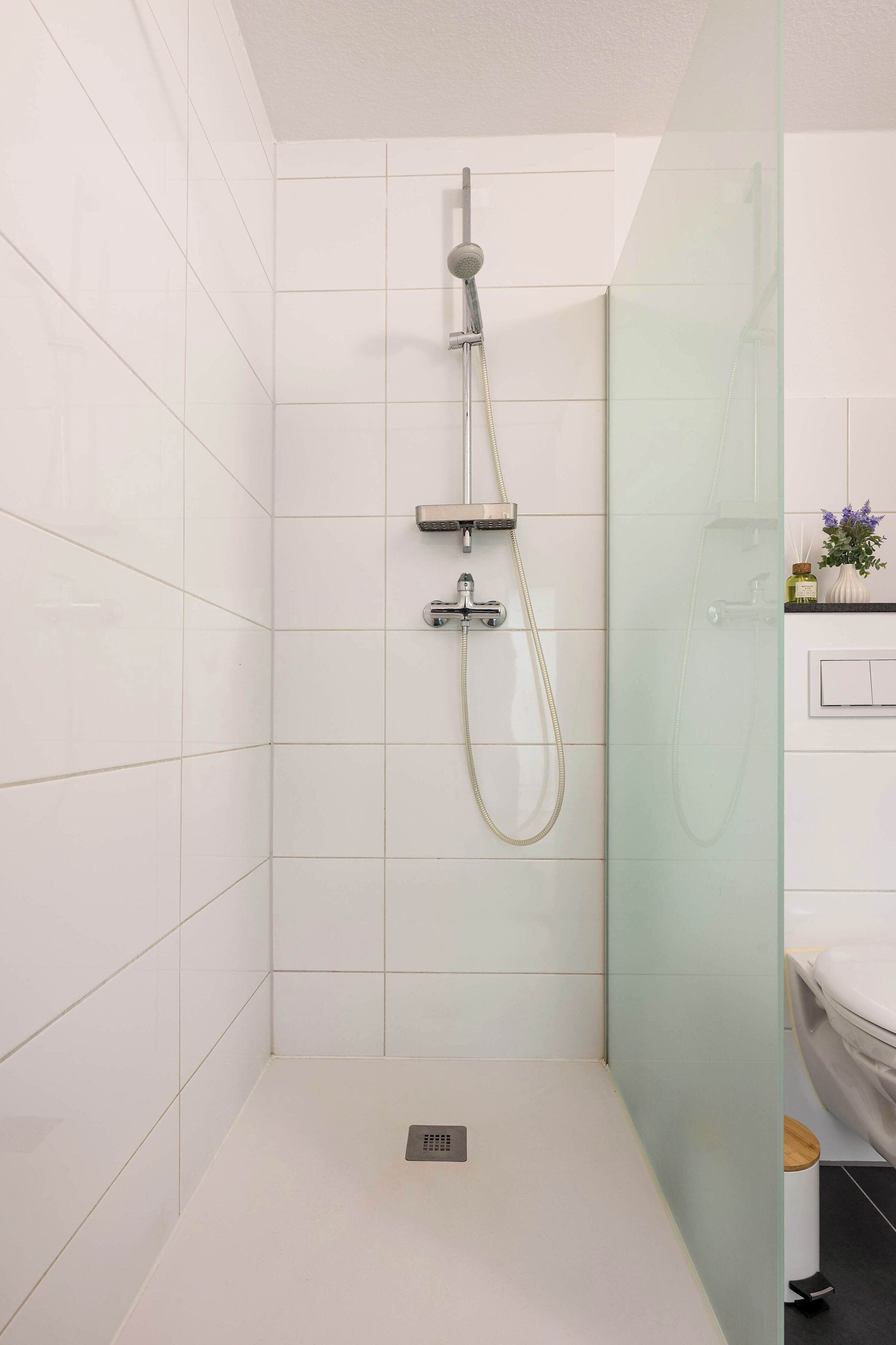 A modern bathroom with white tiles, a glass shower enclosure, and a white sink.