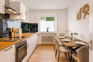 Une cuisine moderne avec des plans de travail en bois, des appareils en acier inoxydable et un coin repas avec une table dressée pour quatre personnes.