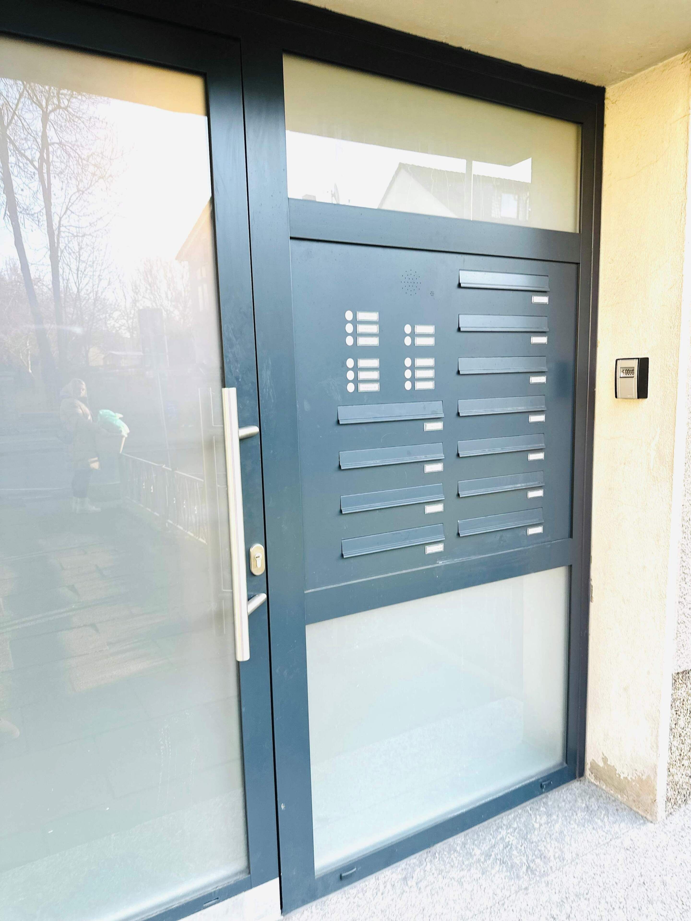 A metal gate with a handle and a keypad lock, leading to a building with a glass door.