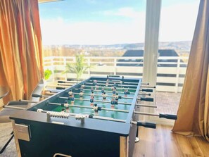 Et bordfodboldspil i et rum med udsigt til et fjerntliggende landskab gennem store vinduer.