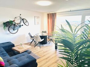 Ein modernes Wohnzimmer mit einer Couch, einem Esstisch, Stühlen, einem Fahrrad und einem großen Fenster mit Blick.