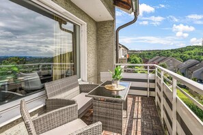 Ein Balkon mit Korbmöbeln, einem Glastisch und Blick auf eine Wohngegend.