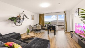 A modern living room with a sofa, a coffee table, a bicycle mounted on the wall, a foosball table, and a TV.