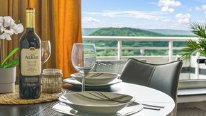 A table with a bottle of wine, a glass, and plates, set against a scenic view.