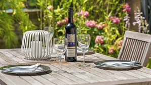 A wooden table set with plates, cutlery, and wine glasses, with a bottle of wine in the center.