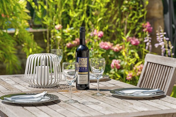 A wooden table set with plates, cutlery, and wine glasses, with a bottle of wine in the center.