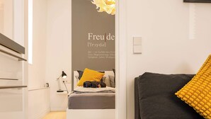 A modern bedroom with a bed, bedside table, lamp, and a sofa with a yellow cushion.
